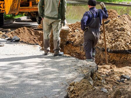 An excavator and three diggers dig a trench to lay a drainage pipe across a public road to drain...