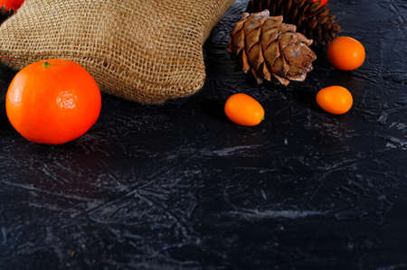 Christmas bag made of coarse burlap, cones, tangerines or oranges, kumquat on a dark background....