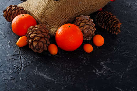 Christmas bag made of coarse burlap, cones, tangerines or oranges, kumquat on a dark background....
