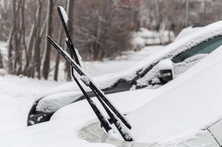 Snow-covered cars with raised wipers in a snow-covered Parking lot in an urban residential areaの写真素材