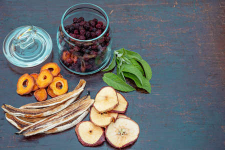 Sliced dried dehydrated apples, apricots and bananas, dried cherries in a glass jar on a dark table. The concept of home preparation of dried fruits in a dehydrator.の写真素材