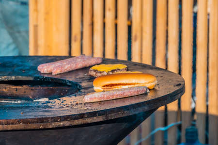 Grilled sausages, steaks, and slices of bread on a large outdoor grill. Barbecue festival in the...