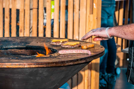 The hands of a gloved man roasting sausages, steaks, and slices of bread on a large outdoor grill. Barbecue festival in the city park.の写真素材