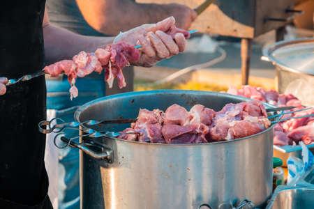 The hands of a man skewering meat on a barbecue skewer. Close-up image of raw meat on a skewer. Street food festival.の写真素材