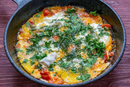 Poached eggs with tomatoes and spices called shakshuka, cooked in a cast-iron pan, on a wooden...