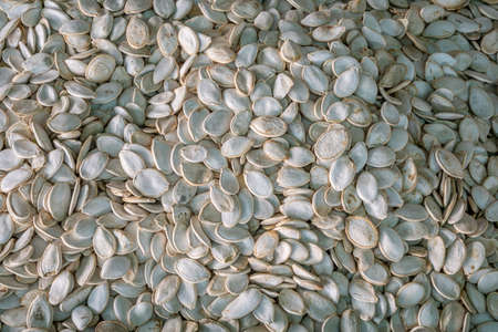 A pile of unpeeled pumpkin seeds, a stand with pumpkin seeds in close-up at the farmer's market....