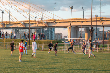 Young football players play football on the field in the city public park on a summer evening.のeditorial素材
