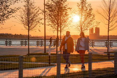 A young man and a woman are walking on a sunny autumn evening by the river on the city embankmentのeditorial素材