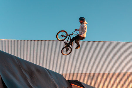 A BMX rider does a stunt on a ramp in a skate park in the city public park for outdoor activitiesのeditorial素材