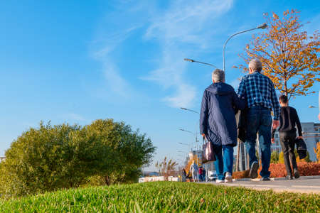 Kazan, Russia - October 14, 2020: A low-angle view of an elderly couple in jeans walking along a pedestrian path on a sunny autumn day against a blue skyのeditorial素材