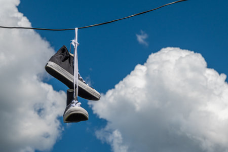 Sneakers hanging on electric wires against a background of blue sky and white clouds.の写真素材