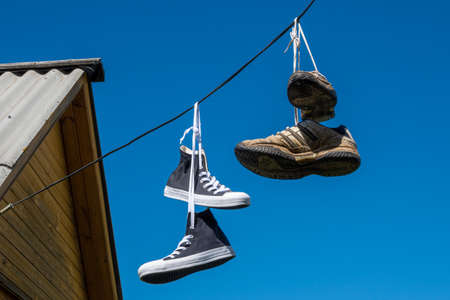 Kazan, Russia - July 25, 2020: New clean and old dirty sneakers suspended by laces on electric wires...