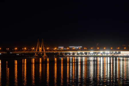 A bridge across the river, illuminated buildings and lanterns on the riverbank, colorful lights of...