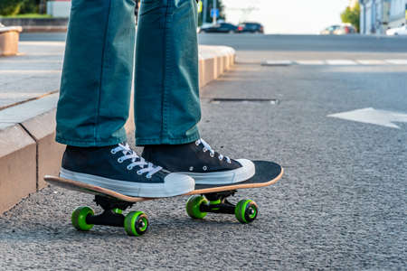 Close-up of men's legs in jeans and sports shoes on a skateboard on a city street at sunset