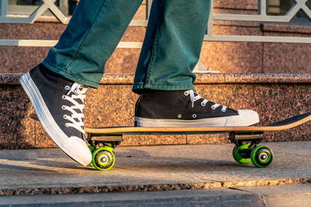 Close-up of men's legs in jeans and sports shoes on a skateboard on a city street at sunset