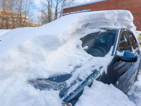 Winter problems of car drivers with snow removal. Cars covered with snow on a city street after a snowfall.の写真素材