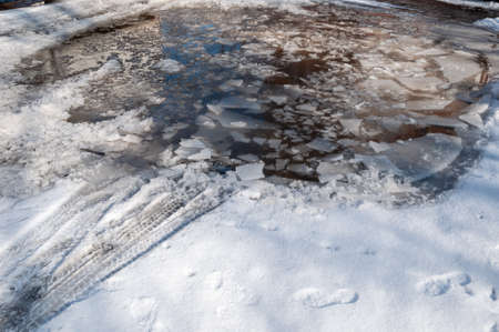 Off-road melted snow and deep thawed areas with slippery ice on the edges. Puddles on a snowy road in early spring.の写真素材