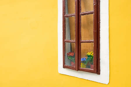 An old window with flowers on the windowsill against the background of the yellow wall of the house.の写真素材