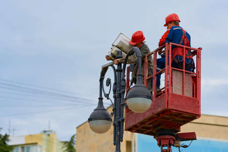 Sochi, Russia -April 20, 2021. Two workers in a lift cradle repair a spotlight on a lamppost. Work...