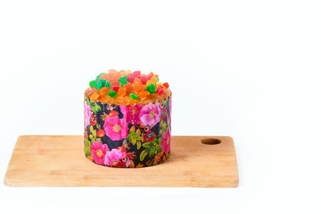 Wooden board with sweet Easter cake with candied fruit on a white background. Delicious dessert.