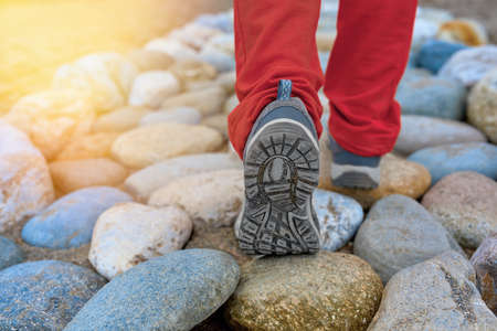 Close-up view of the sneakers of a woman walking on a cobblestone road in sports shoes in the...