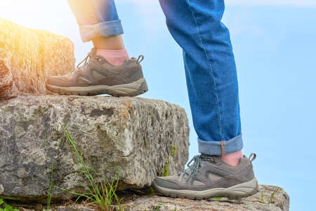 Close-up of the sneakers of a woman walking on stone steps in the rays of the sun against the sky....