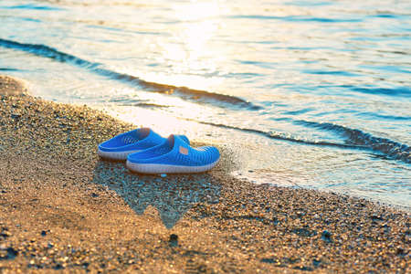 Beach slippers on the sandy seashore in the backlight of the sun. Glare from the sun on the water and sand.の写真素材