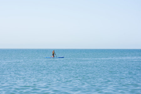 A man alone in a life jacket sits on a SUP board with an oar. Lonely swimmer in the open sea.の写真素材