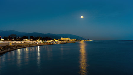 Night view of the Imeretinskiy embankment in the light of the moon. Night lights of lanterns from the shore of the embankment. A beautiful moonlit path is reflected in the sea.の写真素材