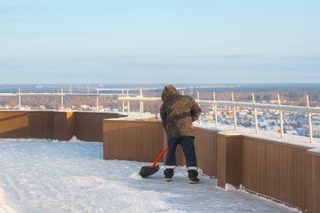 A man removes snow from the roof of a high-rise building with a shovel. City snow removal.の写真素材
