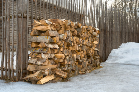 Firewood in a woodpile near the fence in winter. Preparing firewood for the winter to heat a house...