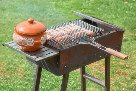 A grill for cooking meat and a clay pot for ready-made pieces. Appetizing meat sausages are fried on grill.の写真素材
