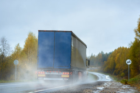 A cloud of splashes and fog when a truck is driving on wet asphalt in the autumn rain. A truck is driving on a wet road. A cloudy autumn day.の写真素材