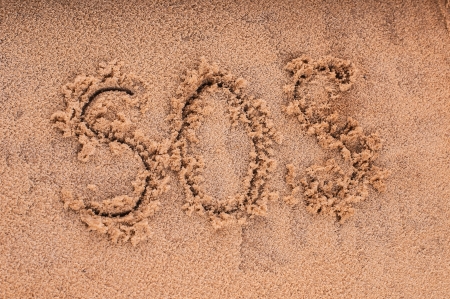 Drawing of "SOS" on the beach sand at the sea.