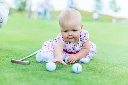 little girl playing on the lawn of golf balls and a stickの写真素材