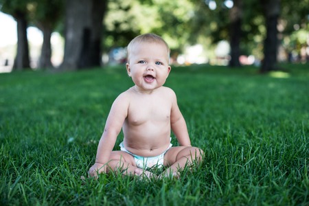 Happy baby with light and fluffy hair sitting on the grass and laughing. Summer and very warm. Happy smile.の写真素材