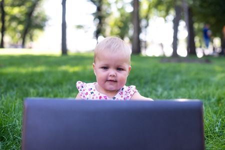 Baby girl sitting on the green grass with laptopの写真素材