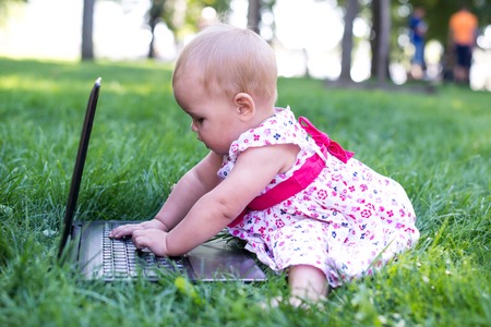 Baby girl sitting on the green grass with laptopの写真素材