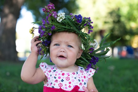 Little girl with a wreath on a head and bouquet in hands on a glade from dandelionsの写真素材