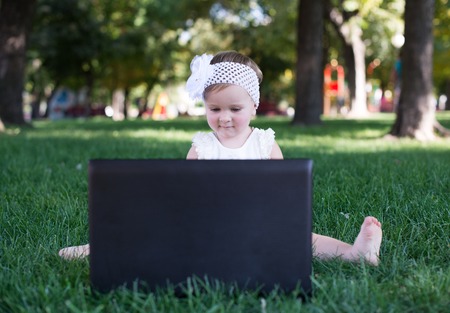 Attractive little girl using laptop in the park lying on the green grassの写真素材