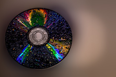 Compact disc with water droplets on the gray isolated background close up