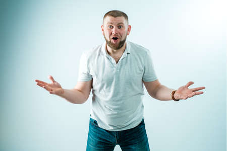 A joyful and charismatic bearded man in a white T-shirt and jeans on a white background, something very surprised and delighted. He spread his arms to the sides and waited for something.の写真素材