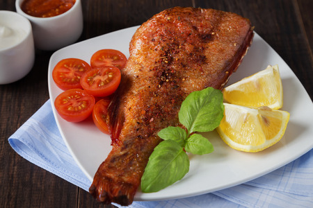 A horizontal photo of a fried perch with tomatoes and basil