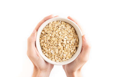 Close up of an oat flakes bowl and a wooden spoon isolated on a white background.