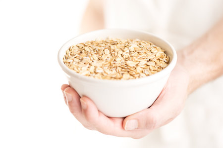 Close-up of an oat flakes bowl held by a man hand on a white backgroundの写真素材