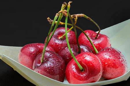 Juicy cherries with water drops in balsa wood bowl on black background