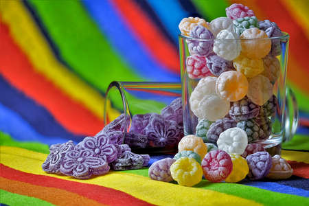 Flavored candies in glass on colorful tablecloth
