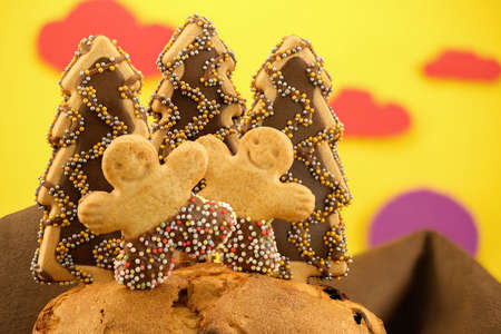 Macro of cute cookies of dolls and trees with chocolate and anise balls, Christmas themed, on sponge cake with simulated background of brown mountains and yellow sky with red clouds and purple sunの写真素材