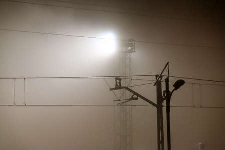 Catenary and spotlight on railway track in fog at sunriseの写真素材