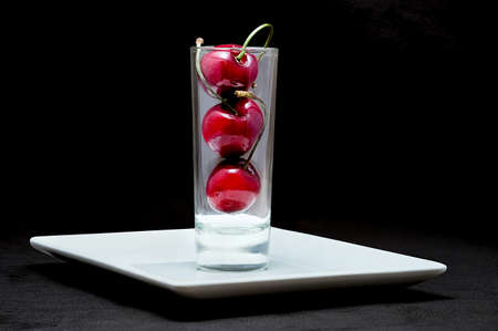 Close up shot of glass with cherries on white plate on black background